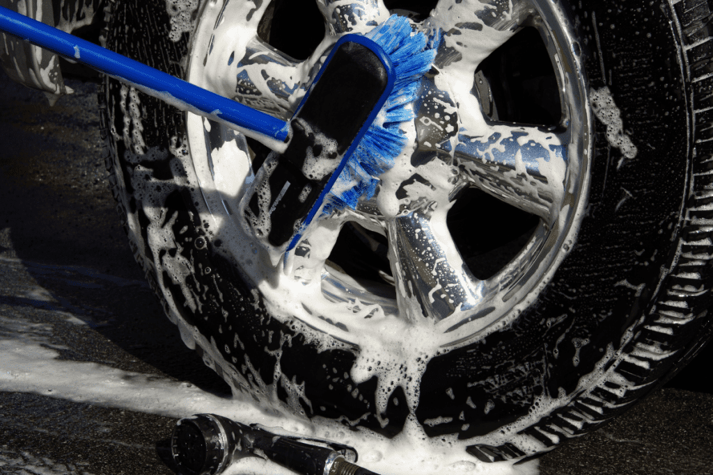 Close-up of an RV tire and wheel being cleaned and dressed by a professional detailer, showing a rich, black tire and sparkling chrome wheel.