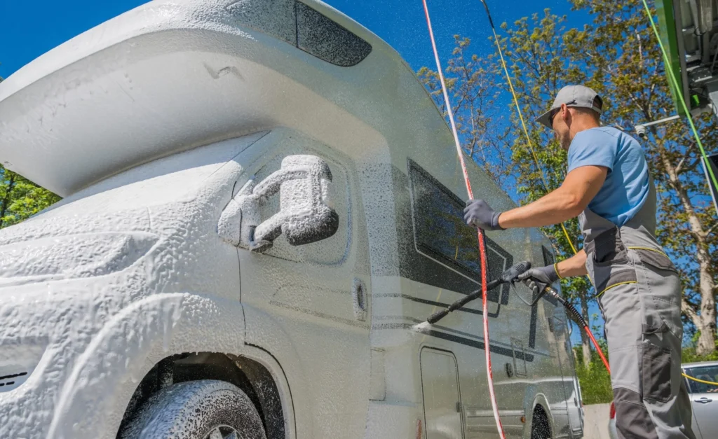 Professional mobile RV exterior wash with water and foam, showing a large, clean recreational vehicle gleaming under sunlight.